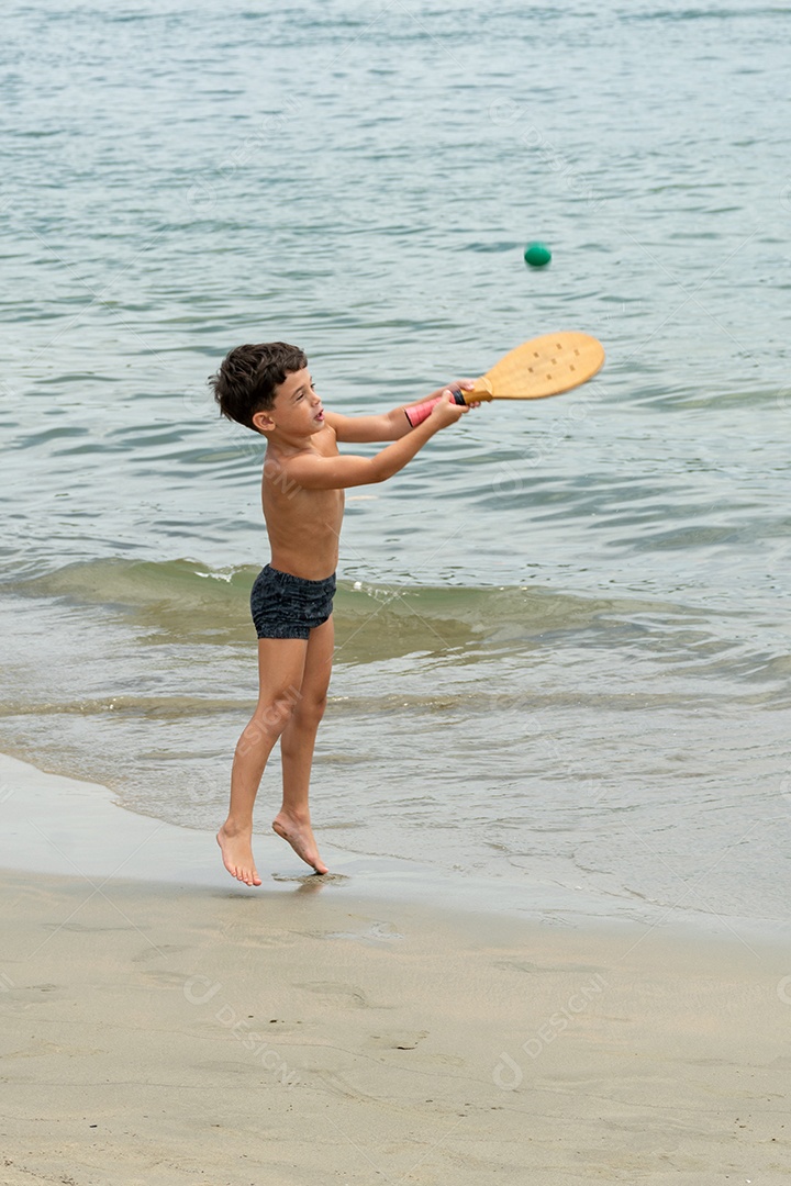Menino de 6 anos jogando um típico jogo de raquete jogado em praias de todo o Brasil.