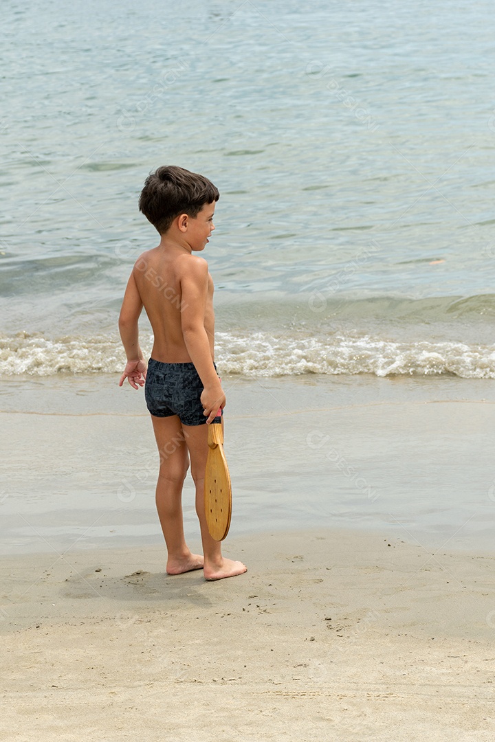 Menino de 6 anos jogando um típico jogo de raquete jogado em praias de todo o Brasil.