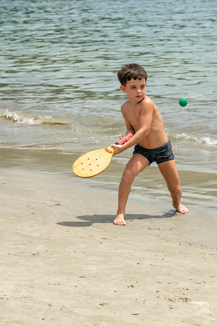 Menino de 6 anos jogando um típico jogo de raquete jogado em praias de todo o Brasil.