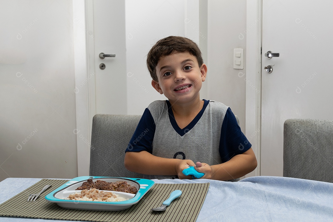 Criança de 6 anos jantando em casa hambúrguer caseiro, arroz branco e feijão