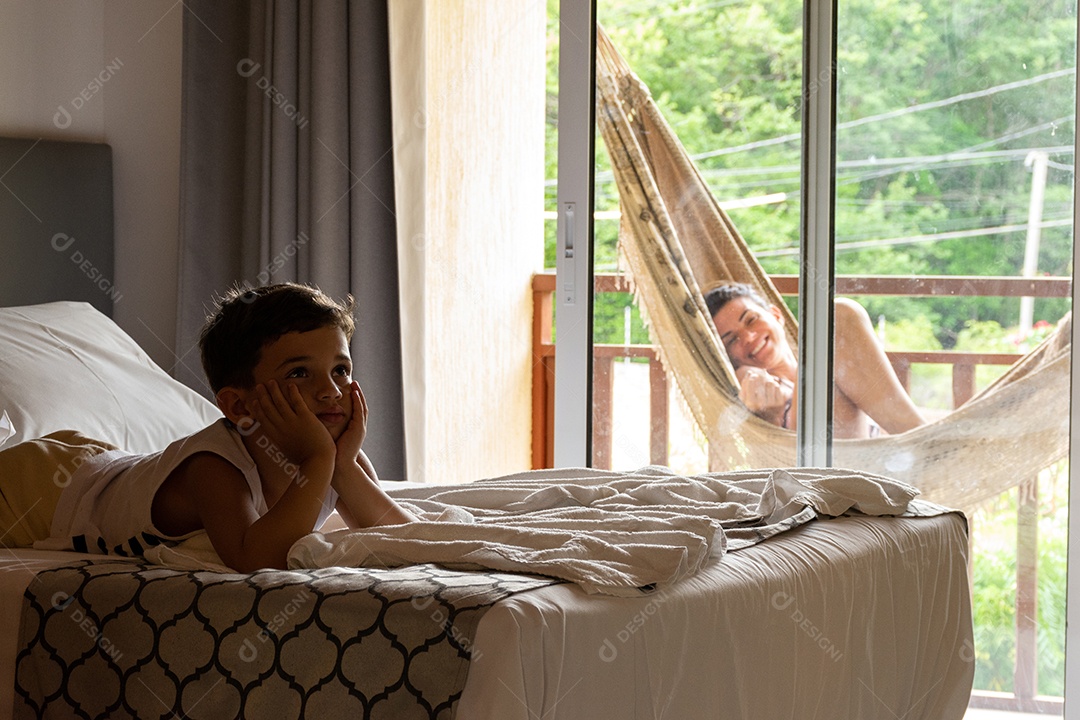 Criança relaxada assistindo TV no quarto do hotel com sua mãe deitada