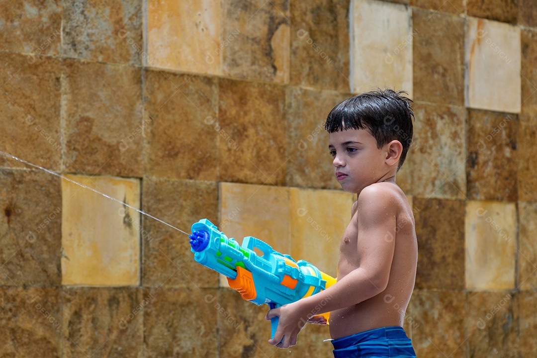 Menino garoto criança brincando segurando arma de agua sobre beira piscina