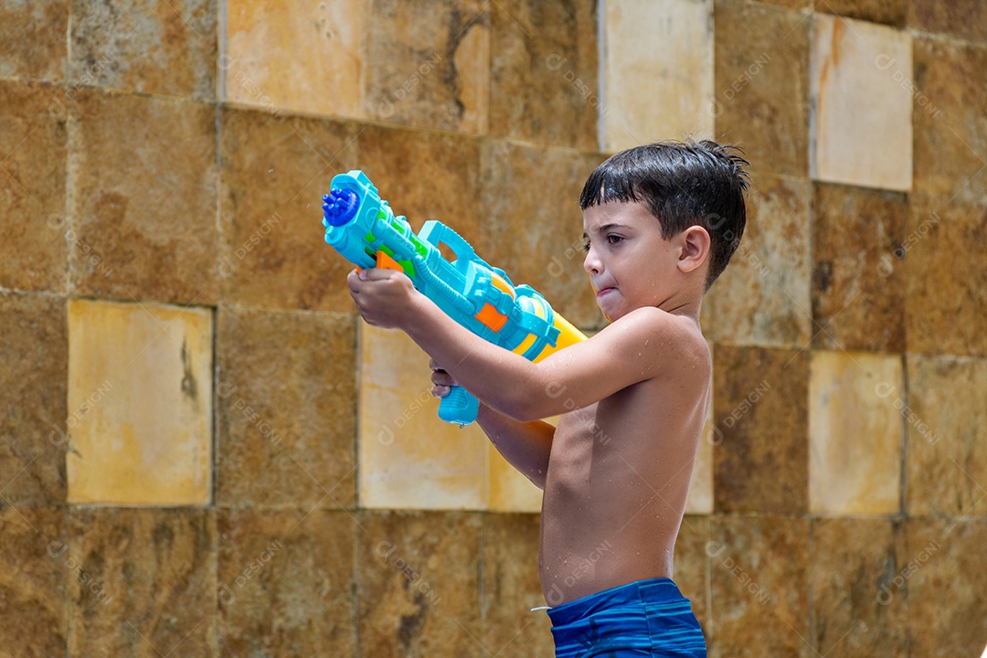 Menino garoto criança brincando segurando arma de agua sobre beira piscina