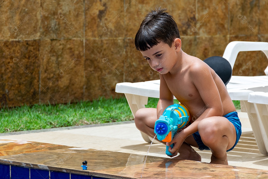Menino garoto criança brincando segurando arma de agua sobre beira piscina