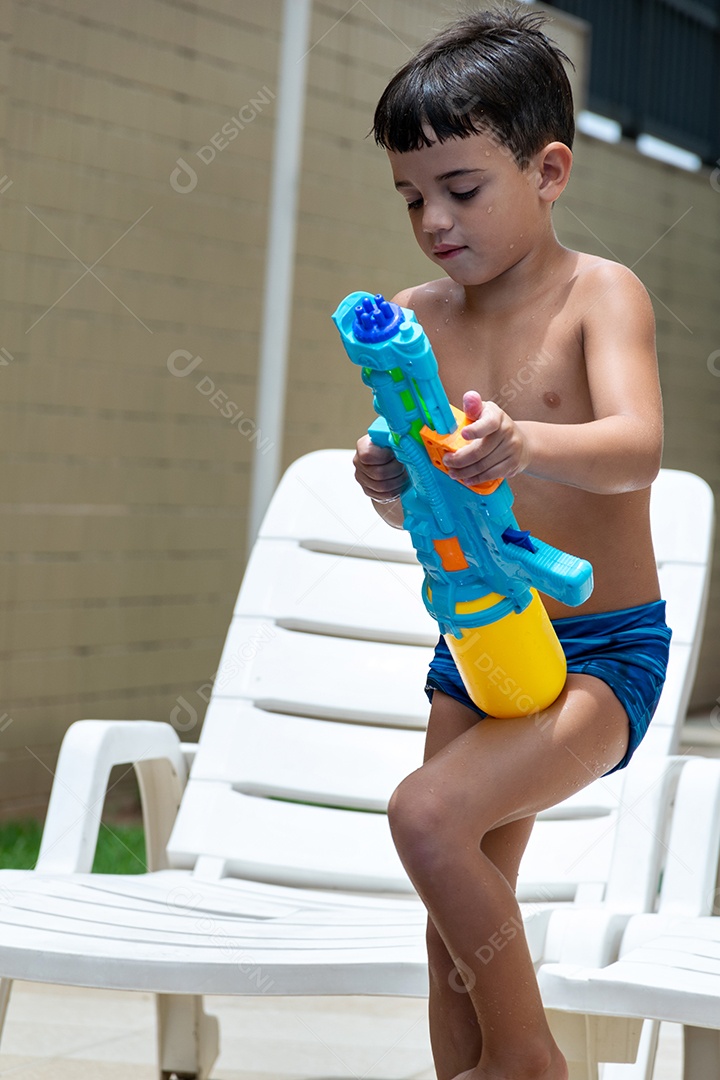 Menino garoto criança brincando segurando arma de agua sobre beira piscina