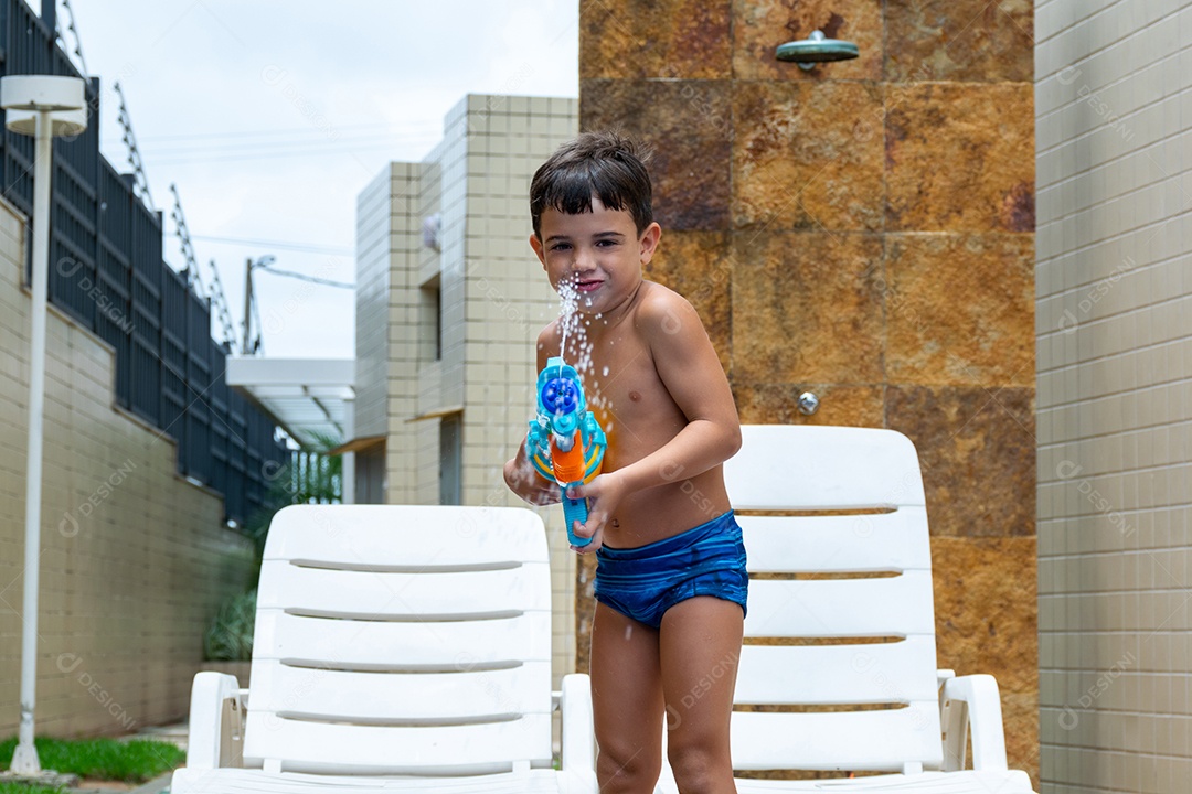 Menino garoto criança brincando segurando arma de agua sobre beira piscina