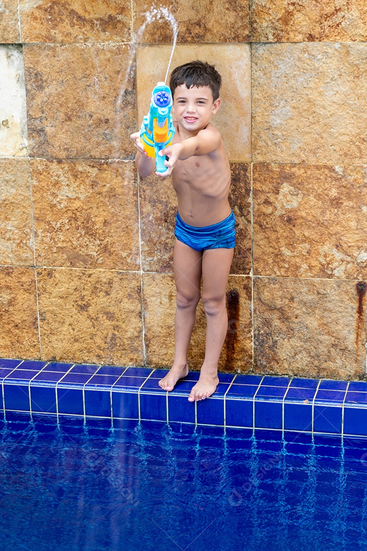 Menino garoto criança brincando segurando arma de agua sobre beira piscina