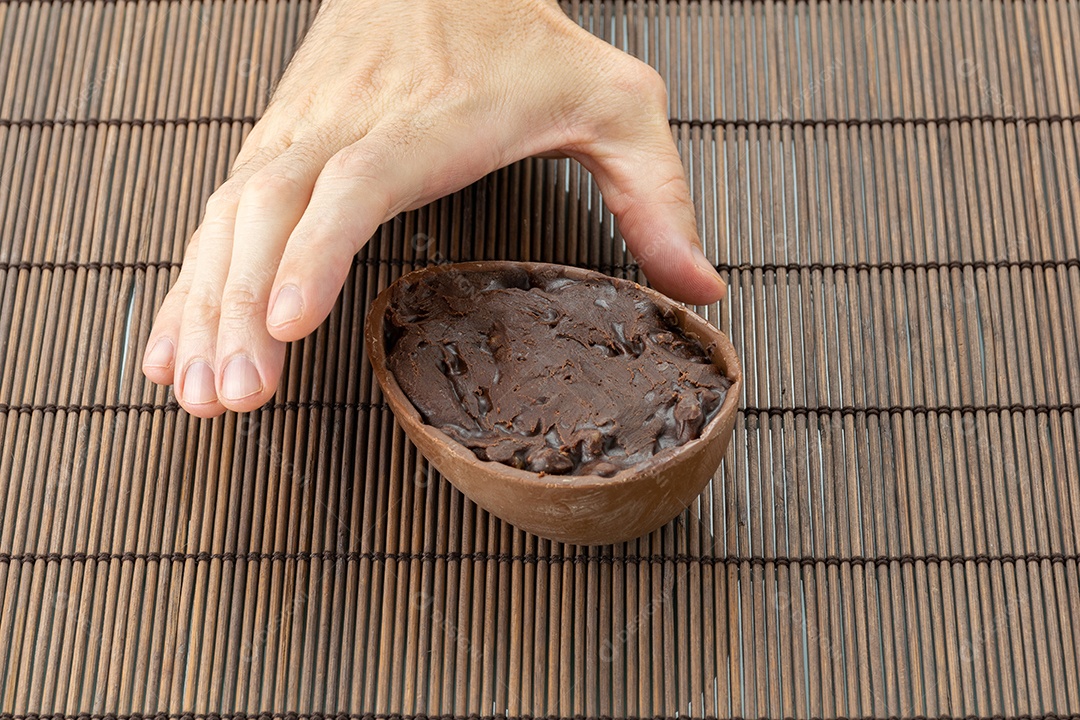 Mão direita de um adulto pegando o ovo de Páscoa de chocolate
