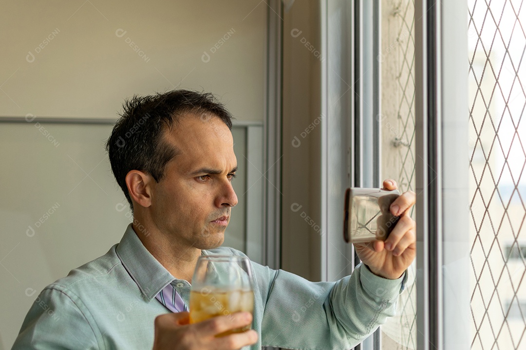 Homem maduro 44 bebendo uísque e assistindo vídeo no smartphone