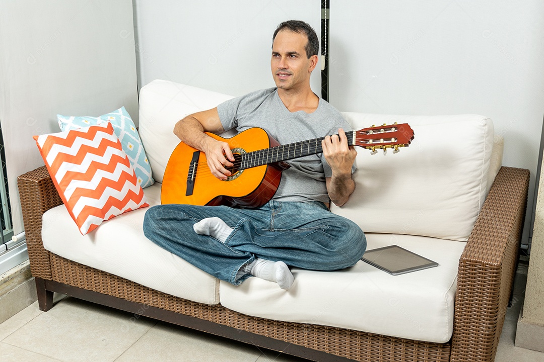 Homem maduro fazendo careta e tocando violão no sofá.