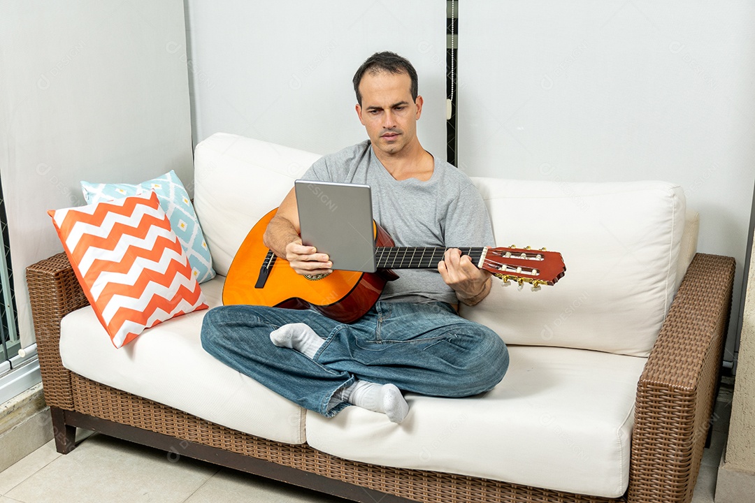 Homem maduro fazendo careta e tocando violão no sofá.
