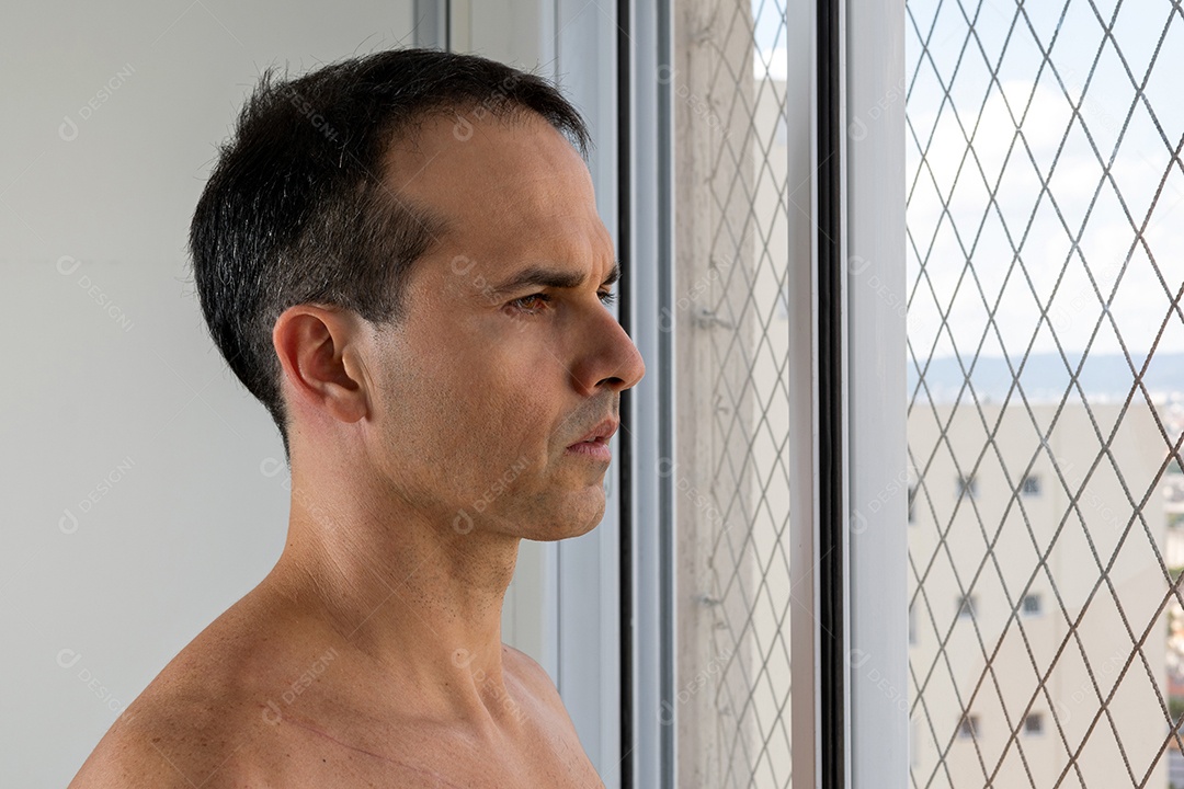 Homem de 44 anos, sem camisa e pensativo, debruçado sobre a janela