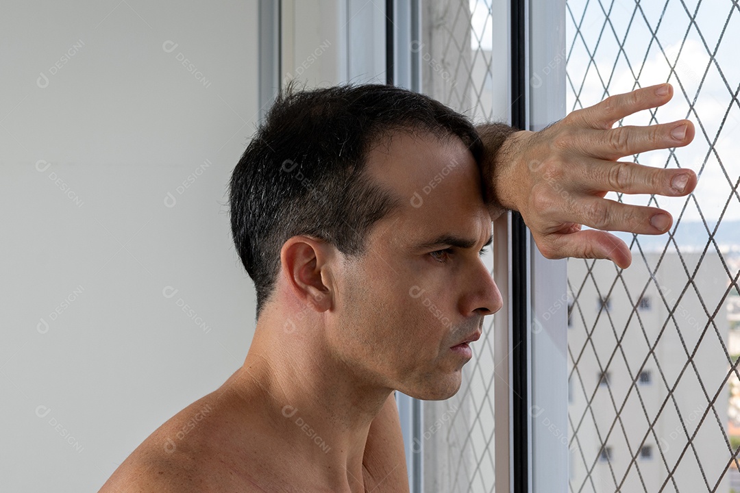 Homem de 44 anos, sem camisa e pensativo, debruçado sobre a janela