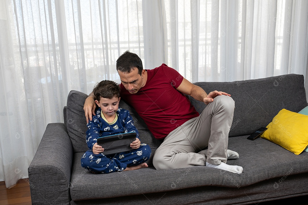 Homem jovem sentado sobre sofá com seu filho sobre conforto de sua casa