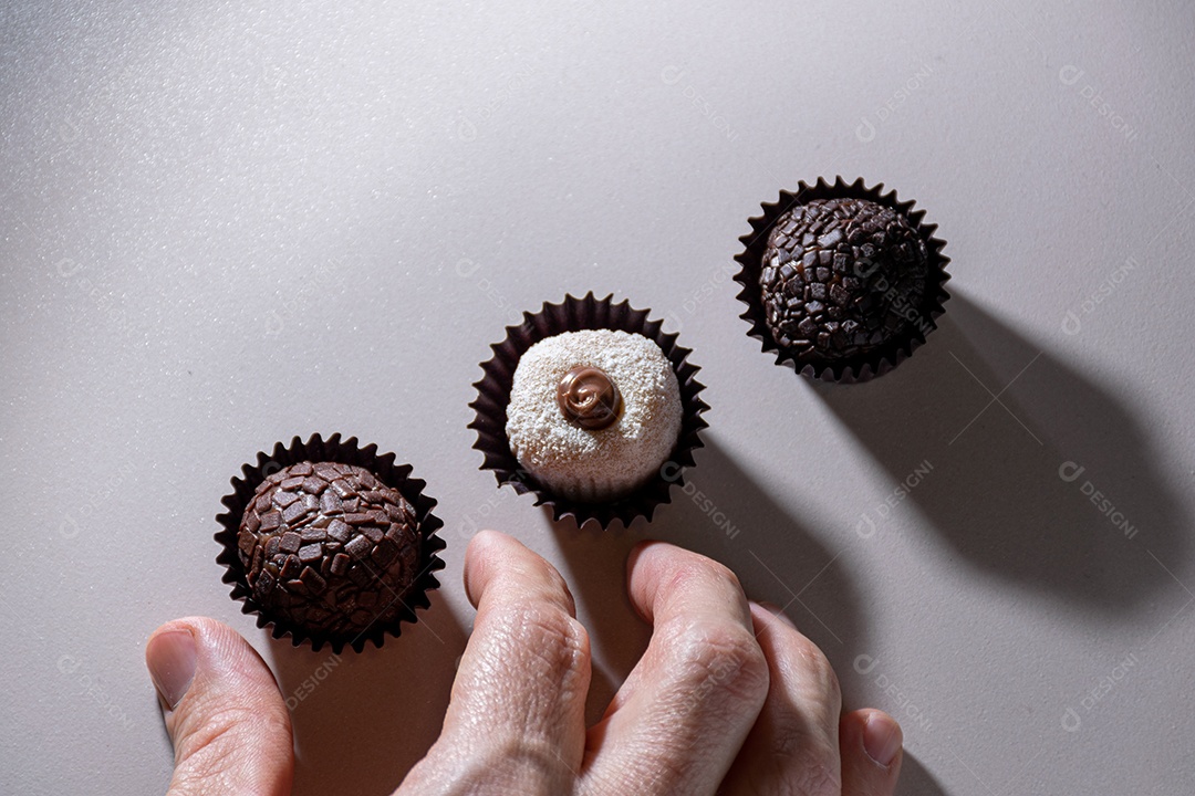 Mão adulta pegando um doce com leite em pó e doce de leite