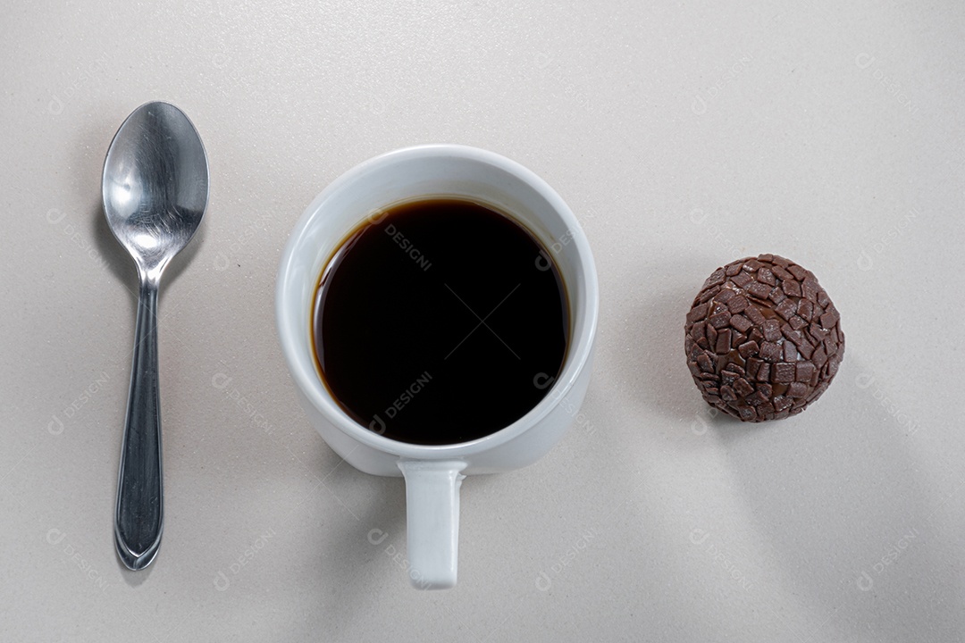 Xícara de café ao lado de uma colher de metal e um brigadeiro
