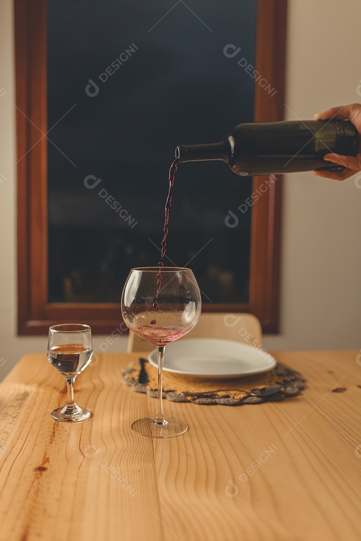 Mãos de pessoa colocando em taça sobre uma mesa de madeira