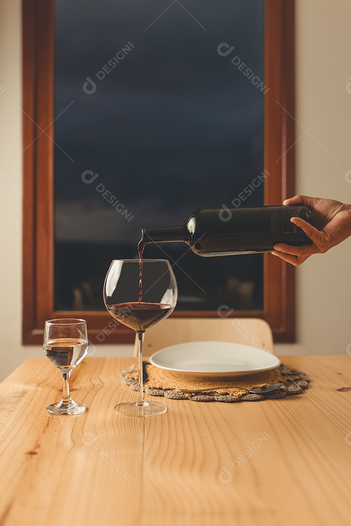 Mãos de pessoa colocando em taça sobre uma mesa de madeira
