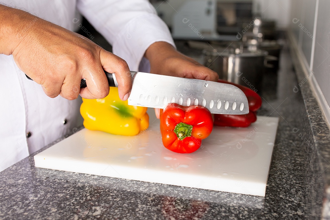 Mãos de chefe de cozinha cortando pimentões sobre uma tabua de madeira