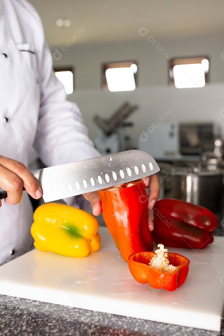 Mãos de chefe de cozinha cortando pimentões sobre uma tabua de madeira