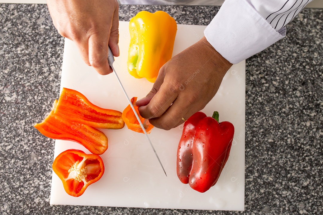 Mãos de chefe de cozinha cortando pimentões sobre uma tabua de madeira