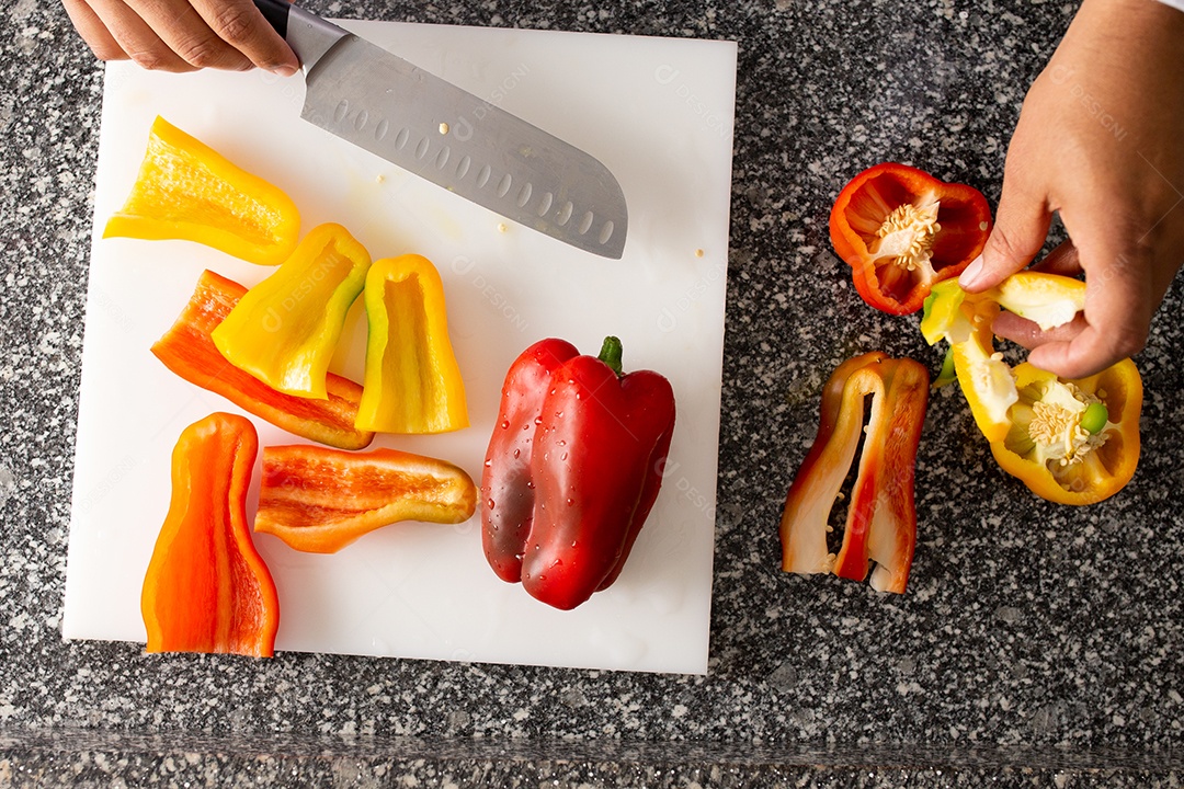 Mãos de chefe de cozinha cortando pimentões sobre uma tabua de madeira