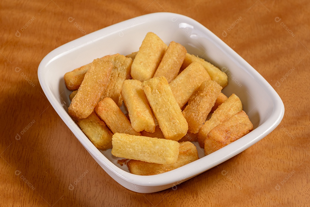 Mandioca frita. Pequena porção de batatas fritas em tigela branca sobre fundo de madeira.