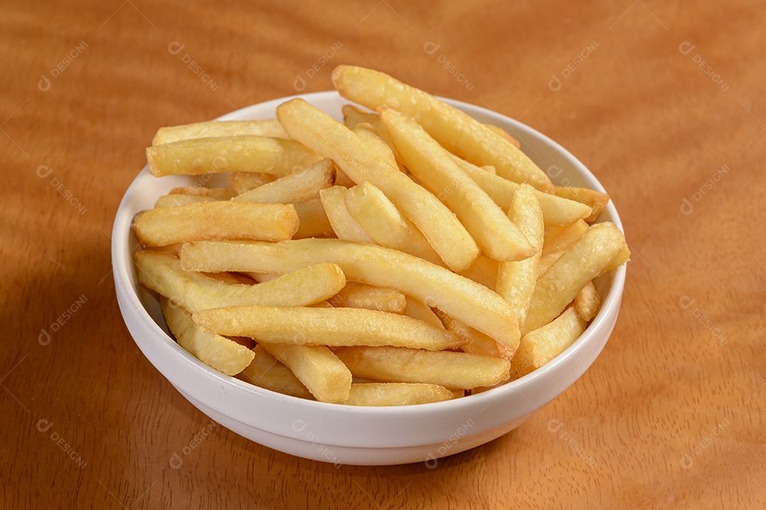 Mandioca frita. Pequena porção de batatas fritas em tigela branca sobre fundo de madeira.