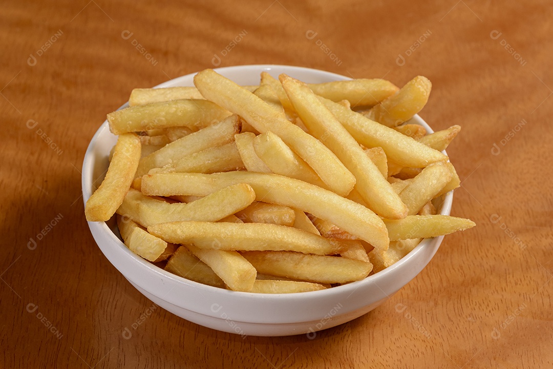 Mandioca frita. Pequena porção de batatas fritas em tigela branca sobre fundo de madeira.