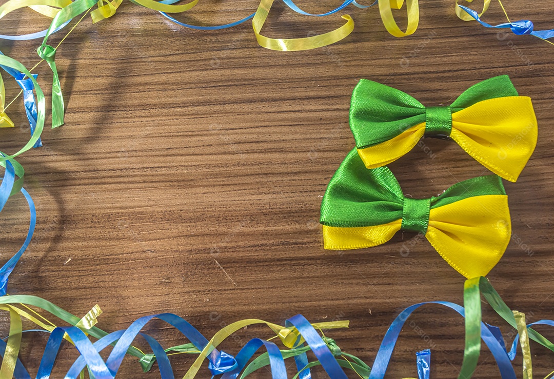 Laço com as cores do brasil sobre uma mesa de madeira com fitas verdes, amarelas e azuis.