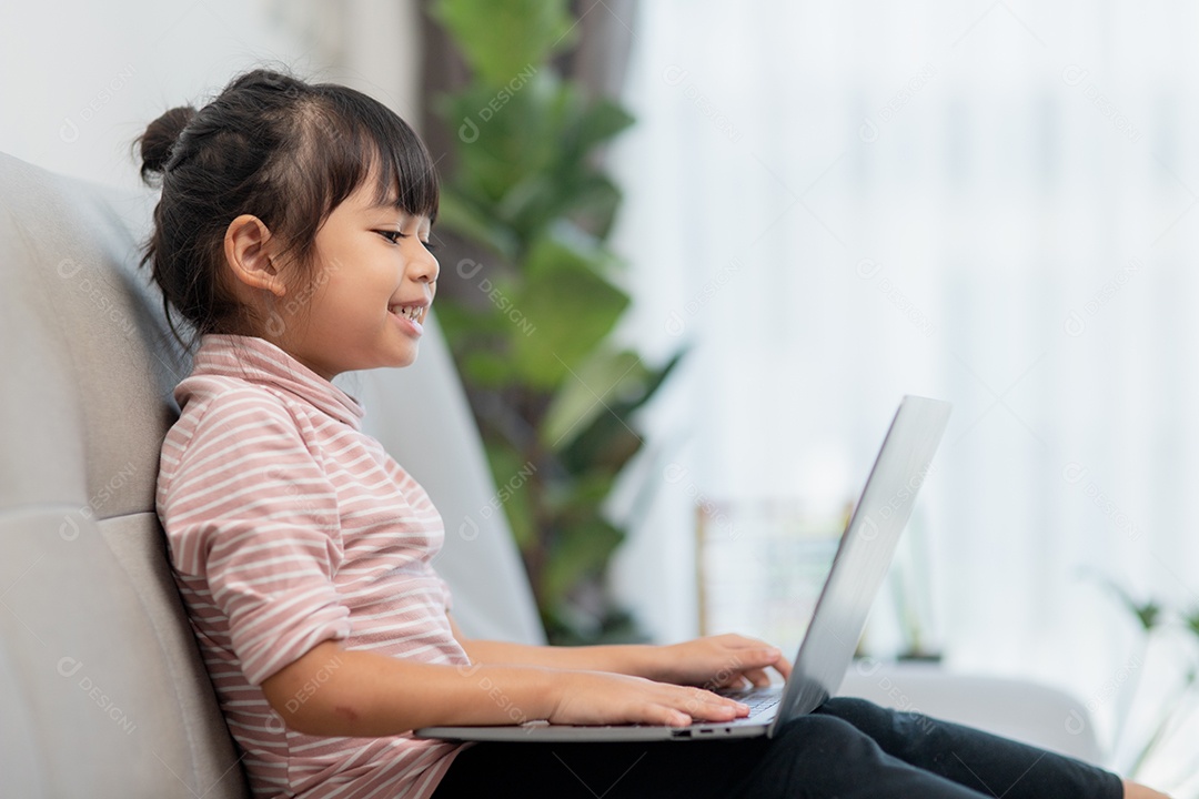 Garotinha asiática usa laptop sentado no sofá