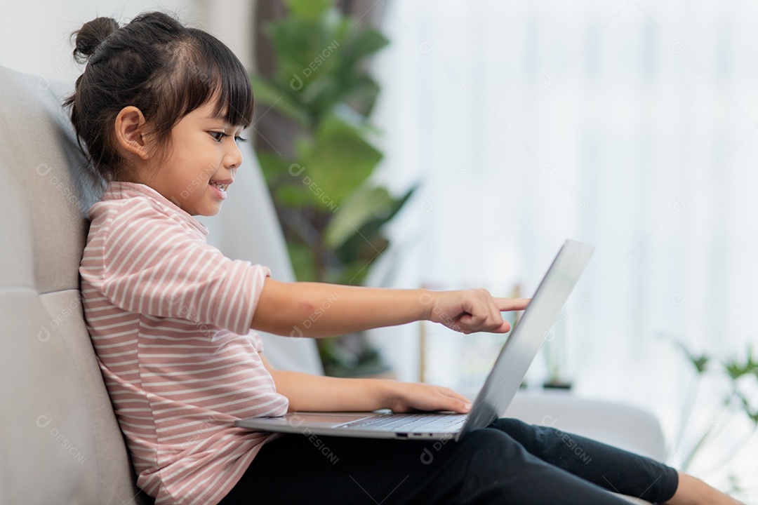 Garotinha asiática usa laptop sentado no sofá