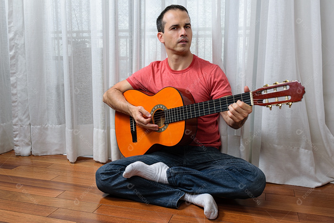 Homem maduro 44 anos sentado no chão e interagindo com um violão e um copo de cerveja.