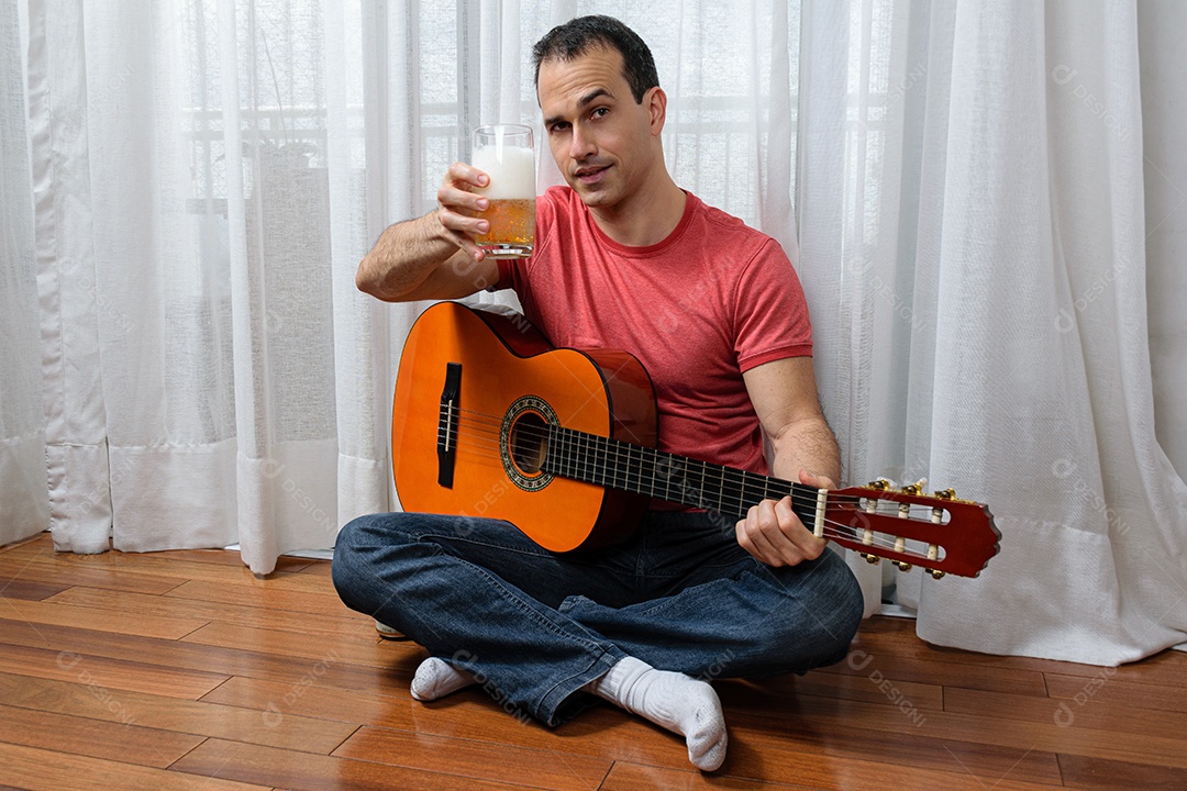 Homem maduro 44 anos sentado no chão e interagindo com um violão e um copo de cerveja.