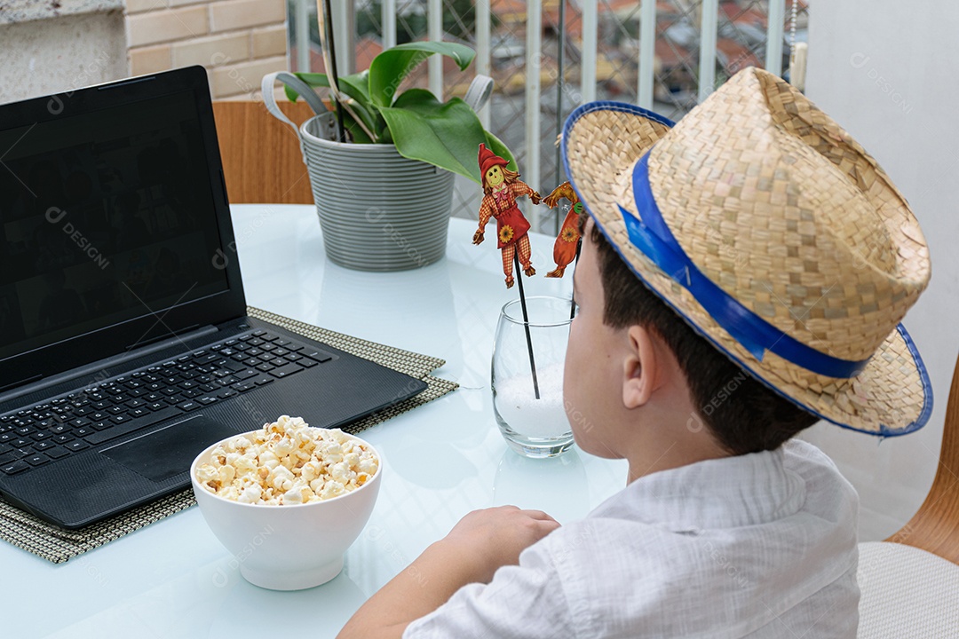 Criança de 7 anos com chapéu de palha e pipoca na frente do notebook