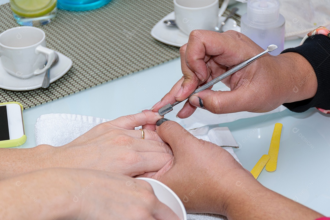 Manicure com palito de madeira com algodão para limpar a cutícula da cliente.