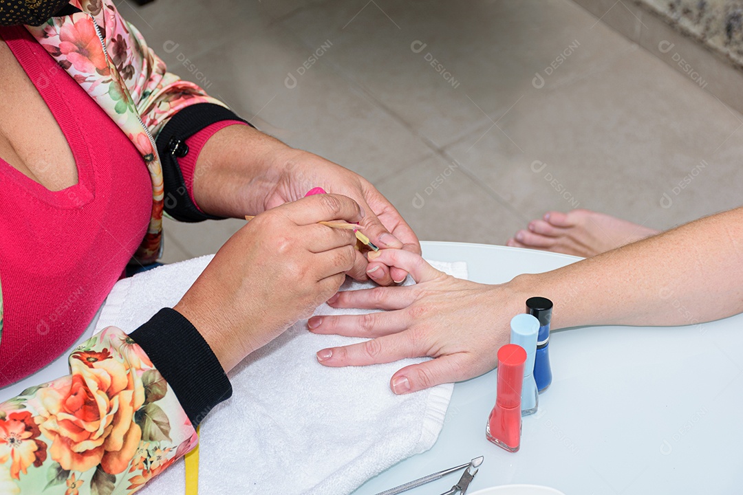 Manicure com palito de madeira com algodão para limpar a cutícula da cliente.