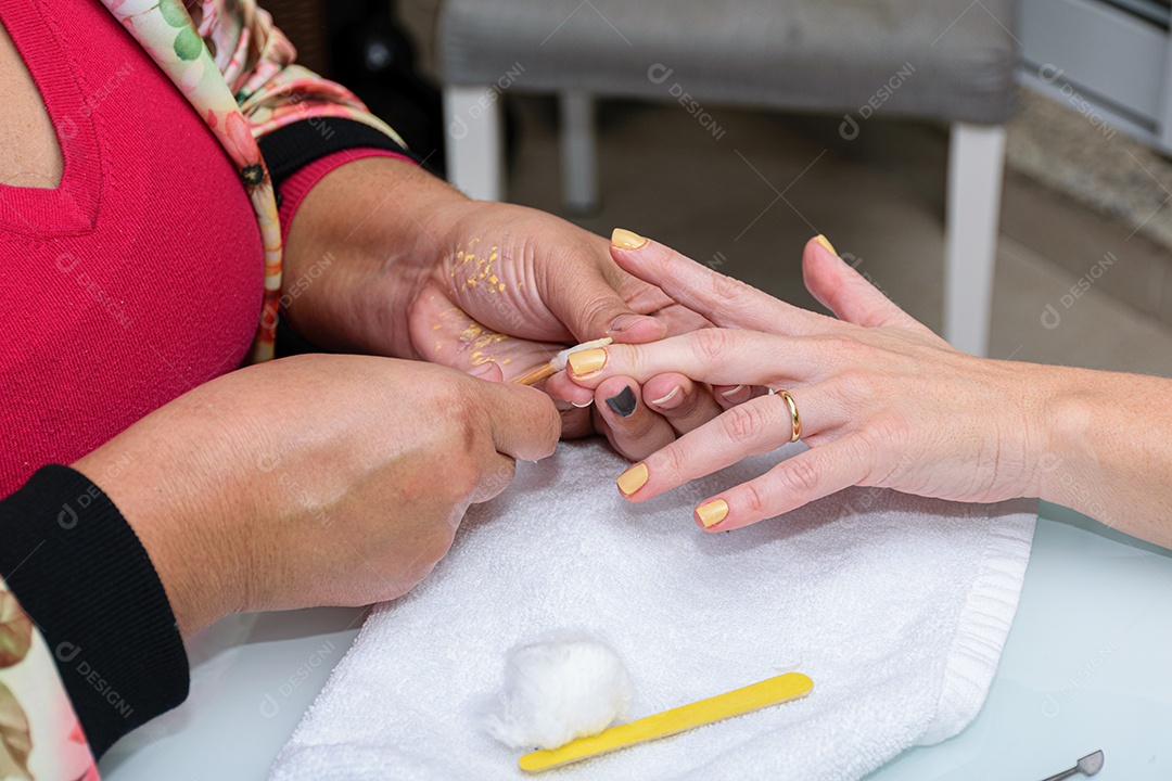 Manicure com palito de madeira com algodão para limpar a cutícula da cliente.