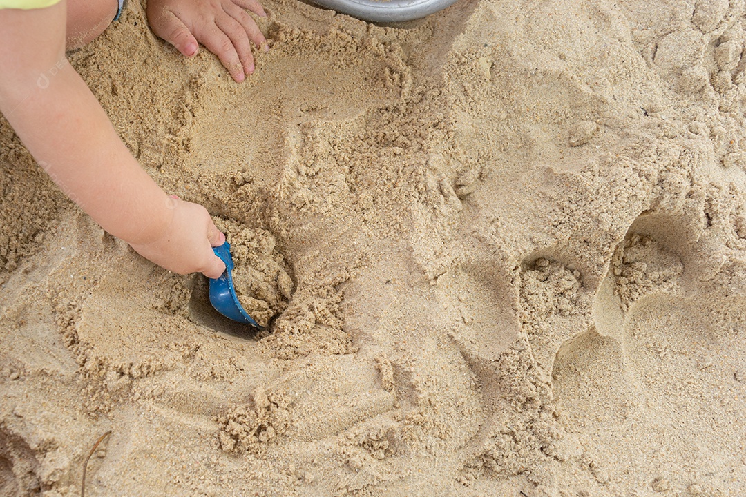 Criança cavando buraco na areia limpa da praia durante o dia ensolarado
