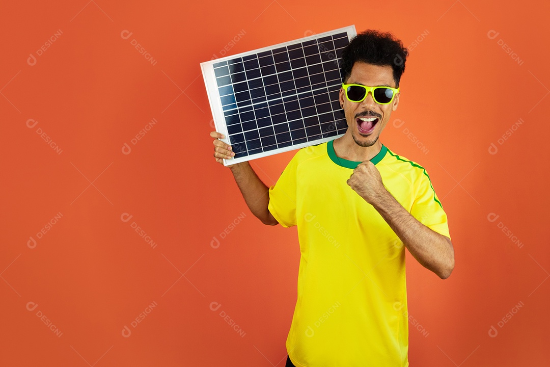 Jogador de futebol - homem negro comemorando segurando painel solar fotovoltaico isolado em laranja