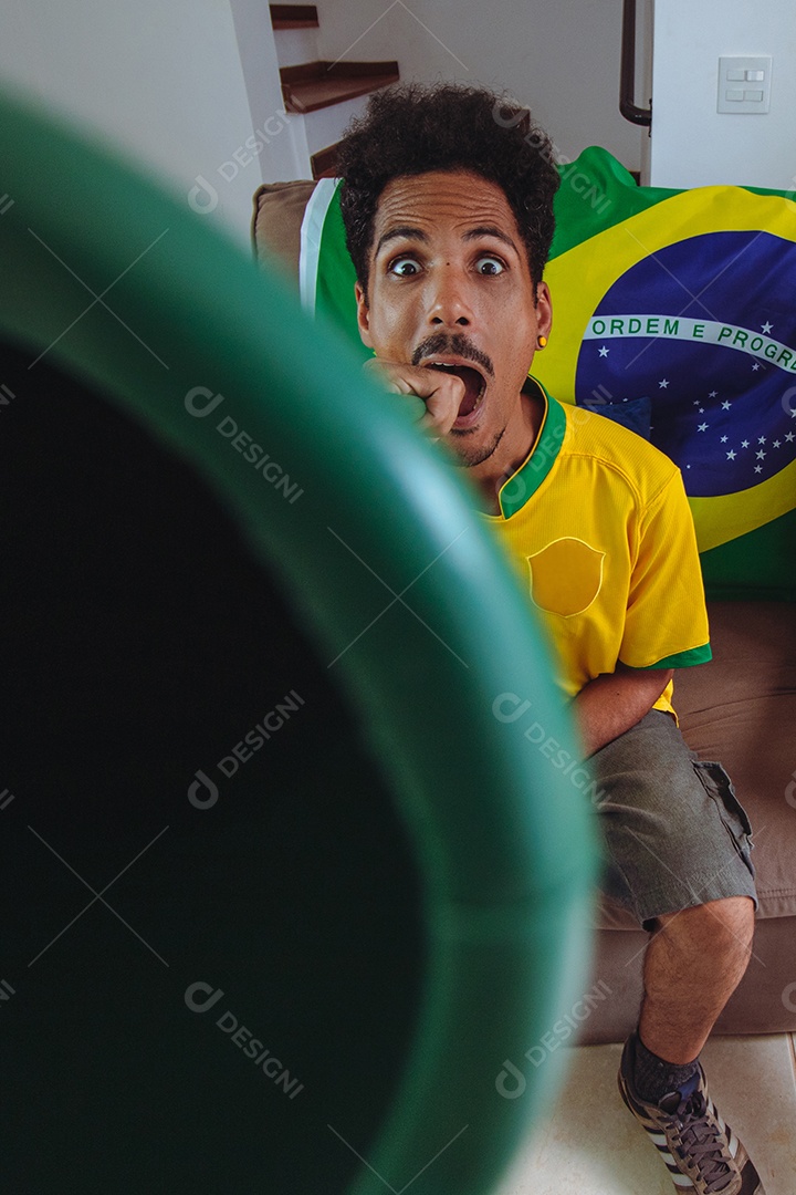 Homem negro com camisa amarela na sala assistindo TV