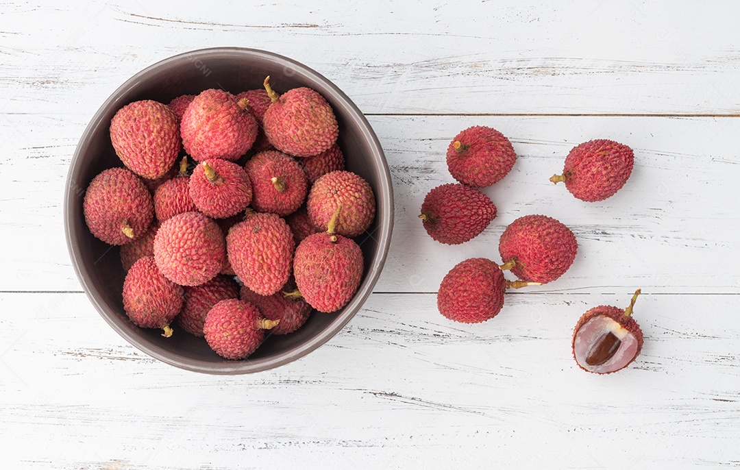 Lichias em uma tigela com frutas cortadas sobre a mesa de madeira.