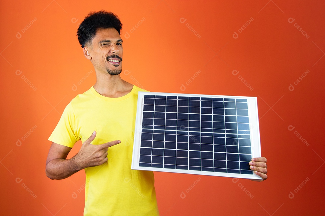 Homem negro bonito segurando um cofrinho e painel solar isolado em laranja.