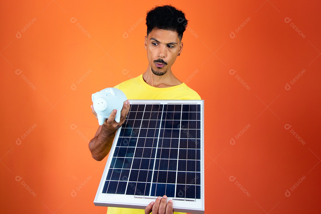Homem negro bonito segurando um cofrinho e painel solar isolado em laranja.