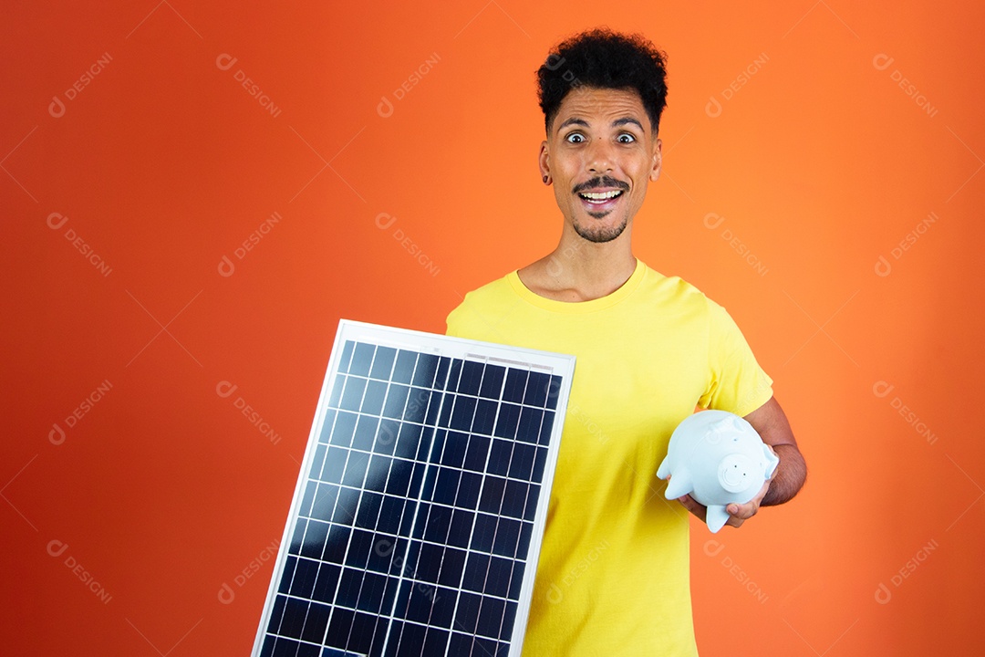Homem negro bonito segurando um cofrinho e painel solar isolado em laranja.