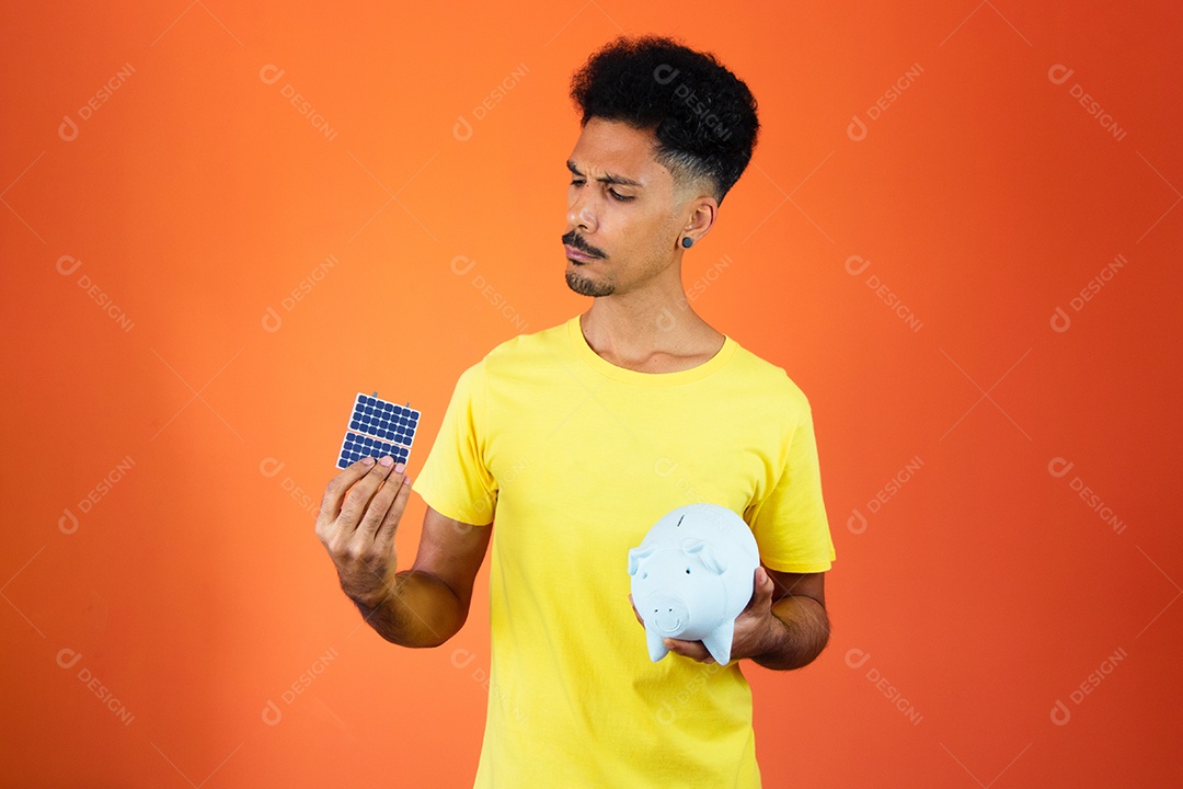 Homem negro bonito segurando um cofrinho e painel solar isolado em laranja.