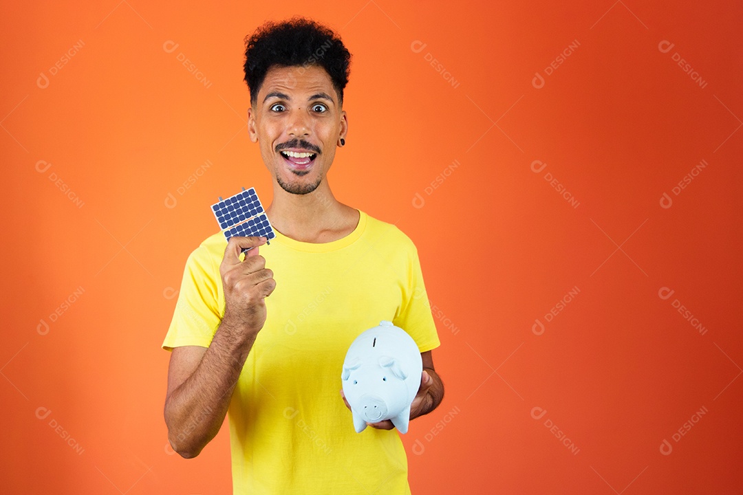 Homem negro bonito segurando um cofrinho e painel solar isolado em laranja.