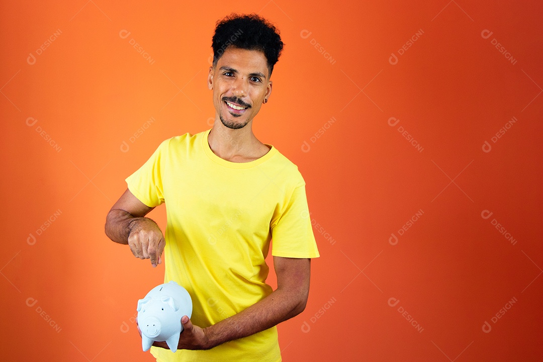 Homem negro bonito segurando um cofrinho isolado na laranja.