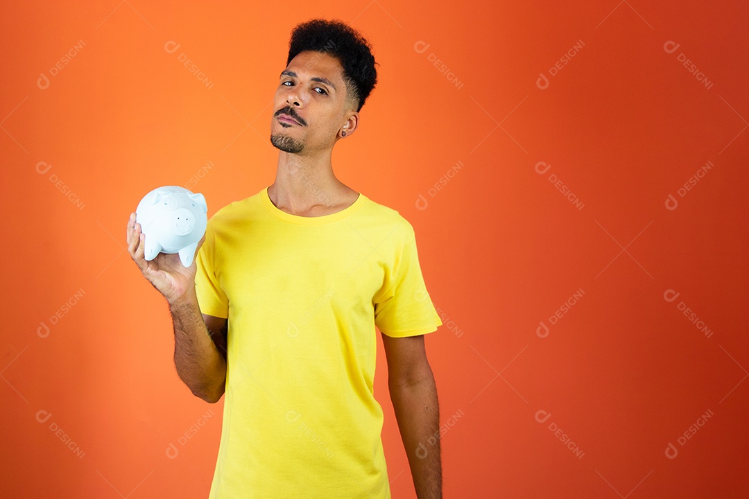 Homem negro bonito segurando um cofrinho isolado na laranja.