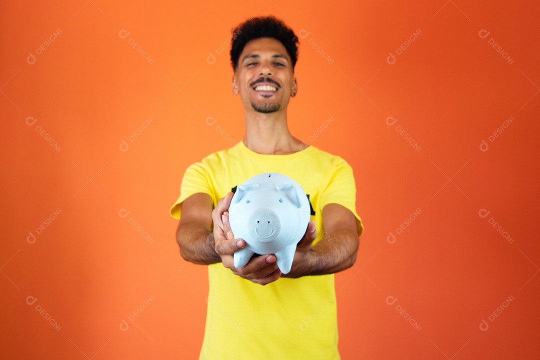 Homem negro bonito segurando um cofrinho isolado na laranja.